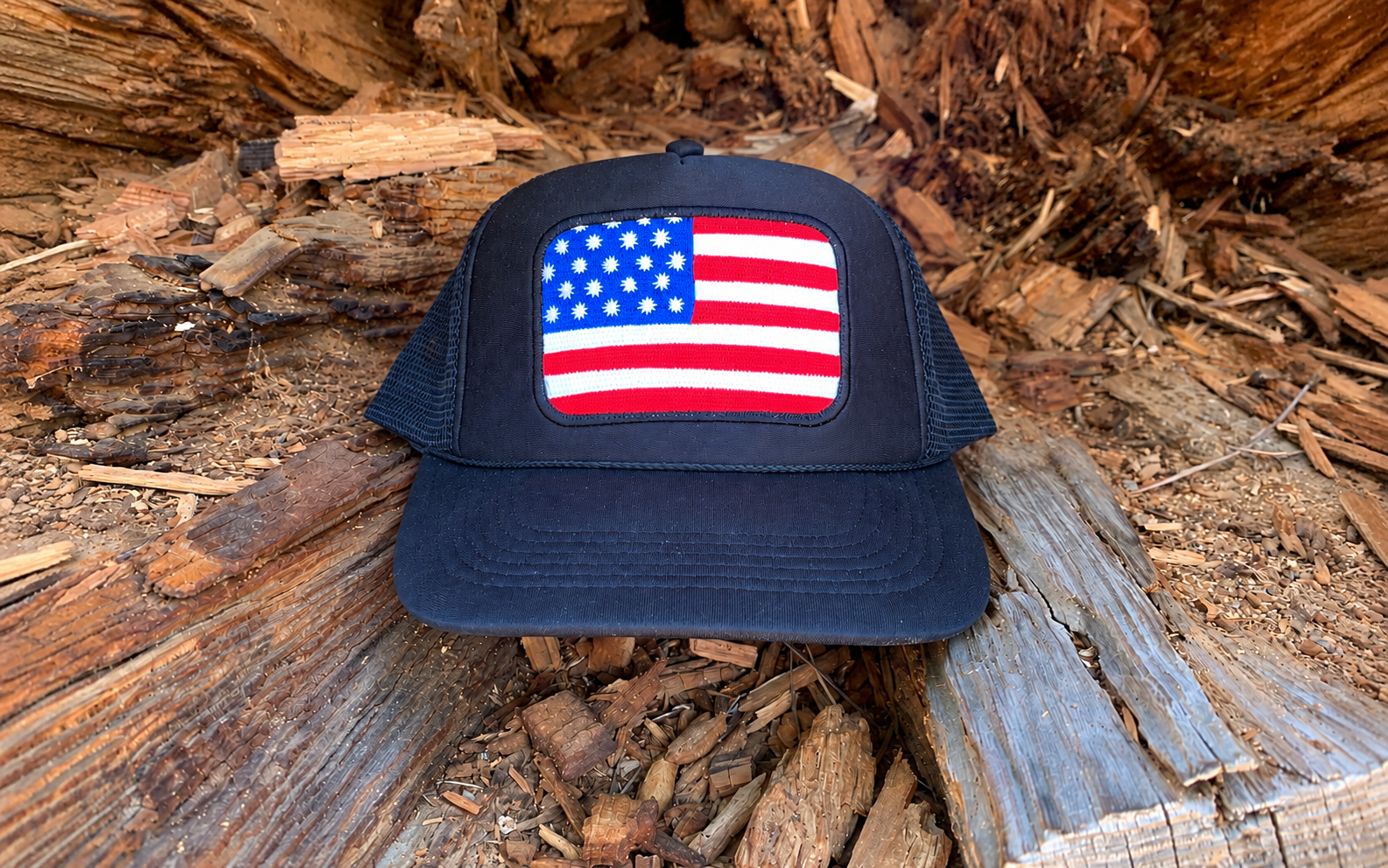 Navy trucker hat with an embroidered American flag patch resting on weathered timber in Idyllwild, California